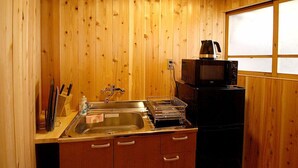 A compact kitchen with wooden walls, a stainless steel sink, a microwave, and a window with frosted glass.