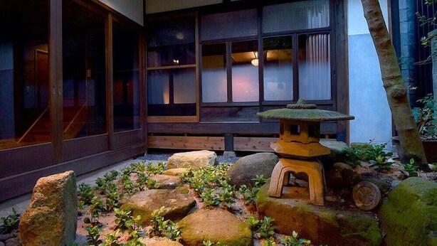 A traditional Japanese garden with a stone lantern, rocks, and a wooden bench.