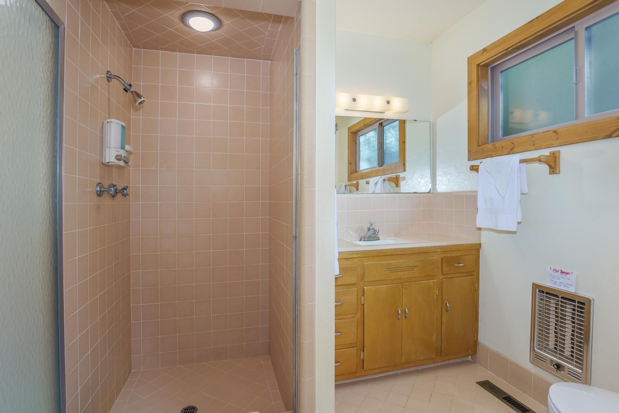 A bathroom with a shower, wooden cabinets, a sink, and a window.