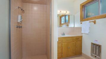 A bathroom with a shower, wooden cabinets, a sink, and a window.