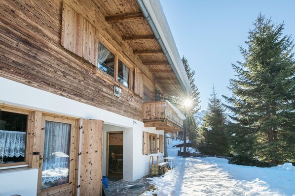 Un bâtiment en bois doté d’un balcon, d’une entrée pavée de pierres et d’un sol recouvert de neige.
