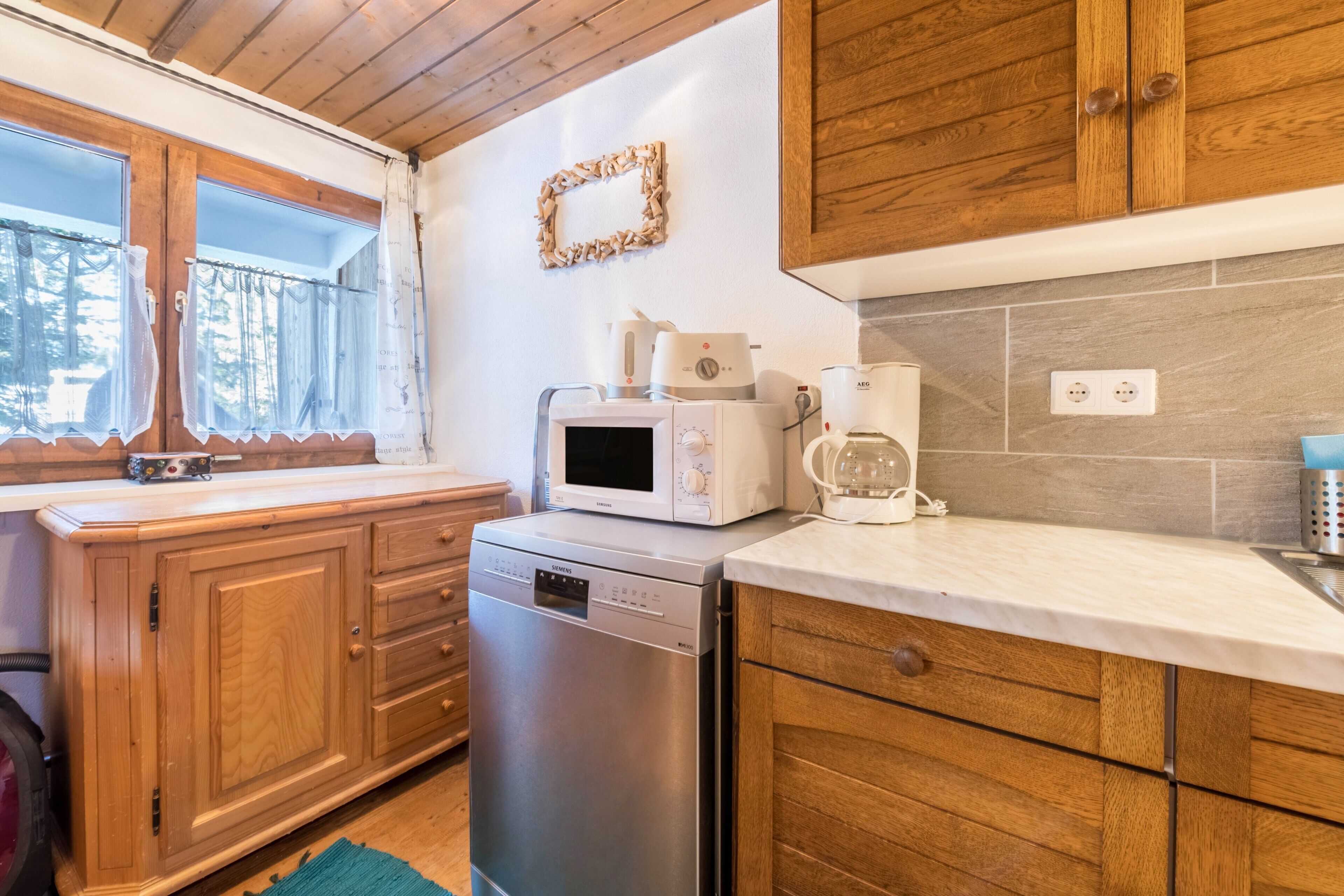 A compact kitchen with wooden cabinets, a dishwasher, a microwave, and a coffee maker.