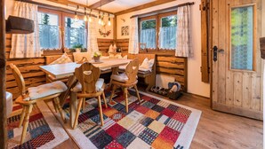 Ein gemütliches Blockhauss-Interieur mit einem Holzespeisetisch, Stühlen, einem bunten Teppich und einer großen Holztür.