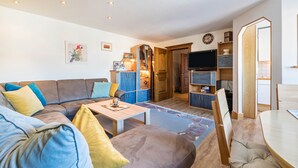 A living room with a sofa, coffee table, and TV. There is a wooden cabinet and a dining table with chairs. - Wieseneck II - Apartment in Fügen (Fügen)