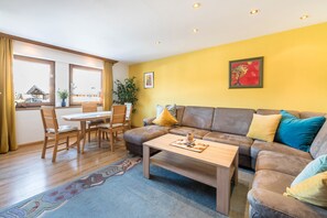 A living room with a sofa, coffee table, and dining area with chairs and a table. - Wieseneck II - Apartment in Fügen (Fügen)
