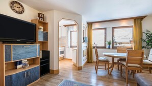 A living room with a flat-screen TV, wooden furniture, a dining area with a table and chairs, and a view of the outdoors through large windows. - Wieseneck II - Apartment in Fügen (Fügen)