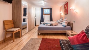 A bedroom with a bed, a chair, a bedside table, a TV, a window with curtains, and a wall-mounted light fixture. - Wieseneck II - Apartment in Fügen (Fügen)