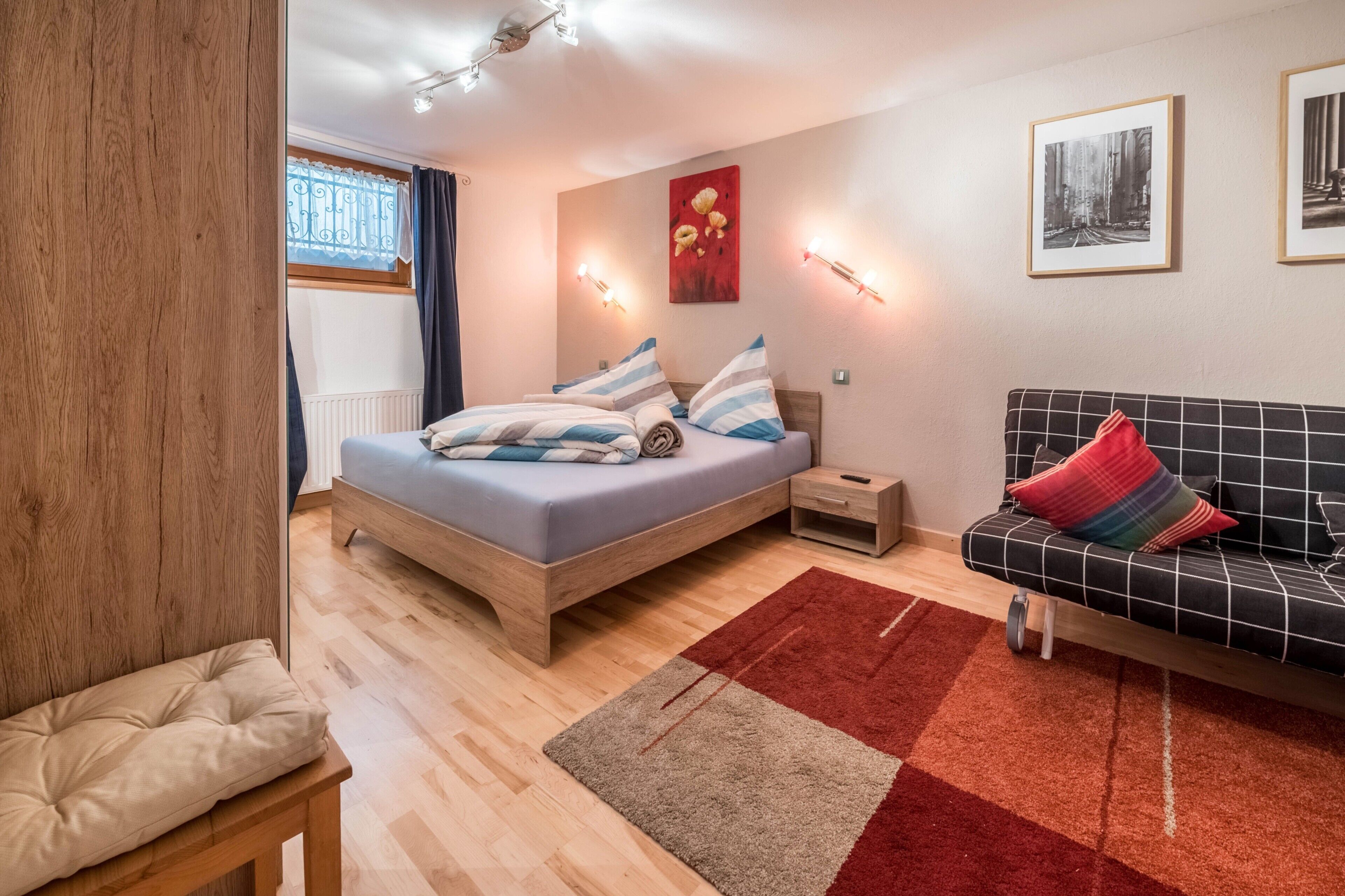 Un dormitorio moderno con una cama de madera, una mesita de noche pequeña, un sofá y un tapete marrón y rojo.