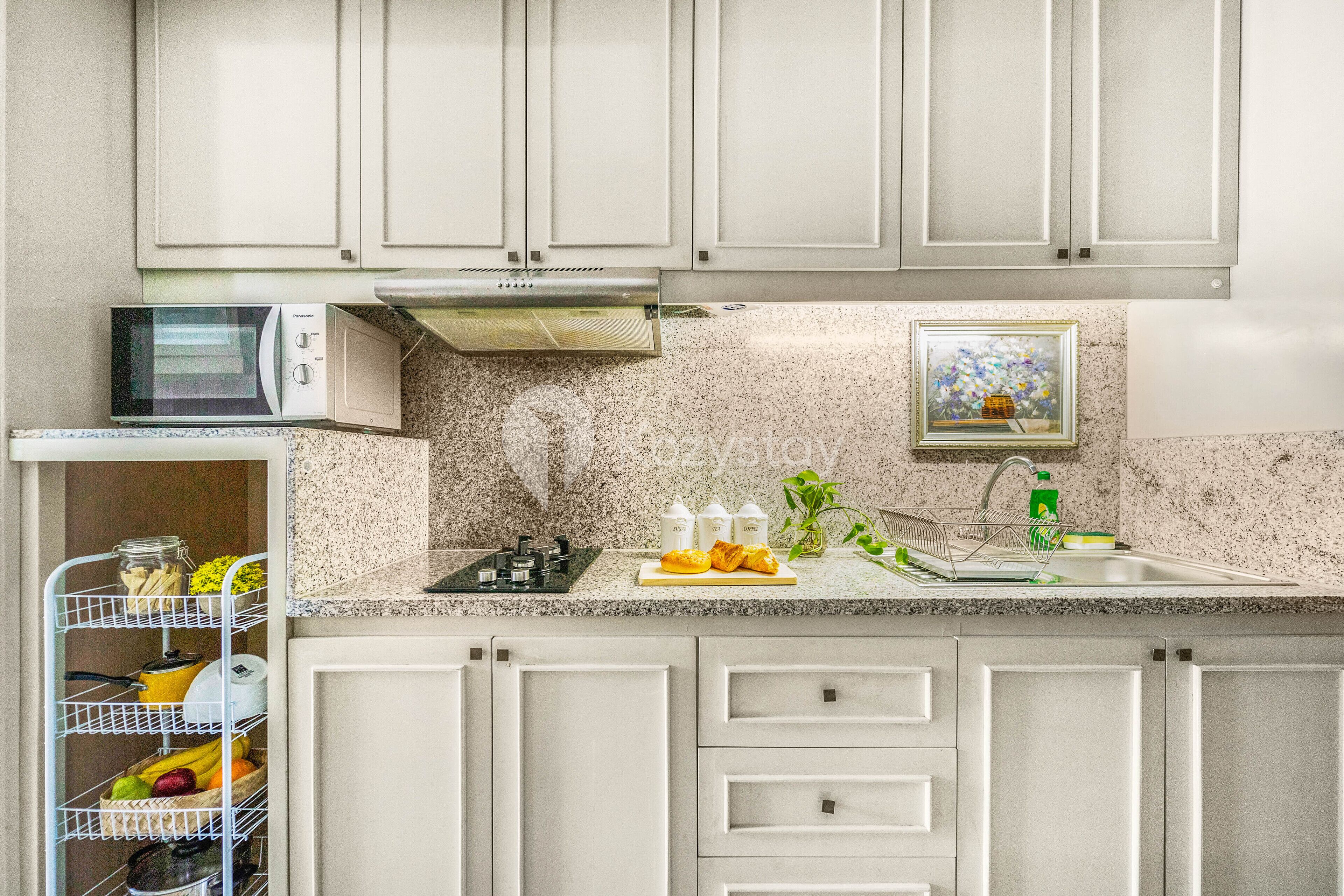 A kitchen with white cabinets, a microwave, a sink, and a dish rack.