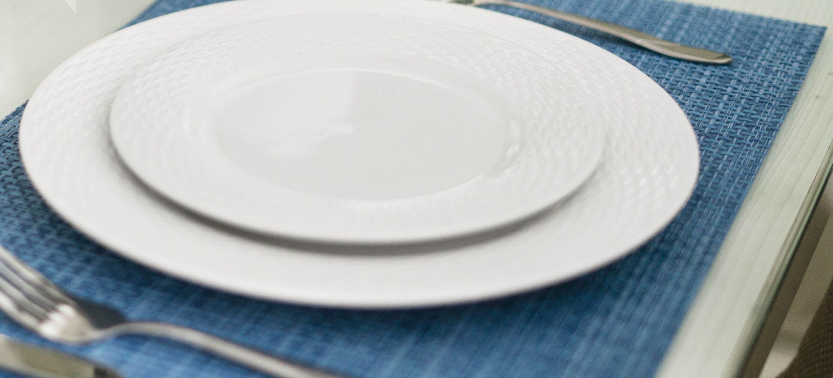 Un plato blanco sobre un mantel azul, con un tenedor y un cuchillo a la izquierda.