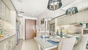 A modern kitchen with white cabinets, a glass dining table, and a chandelier. - CLASSICO by Kozystay (Jakarta)
