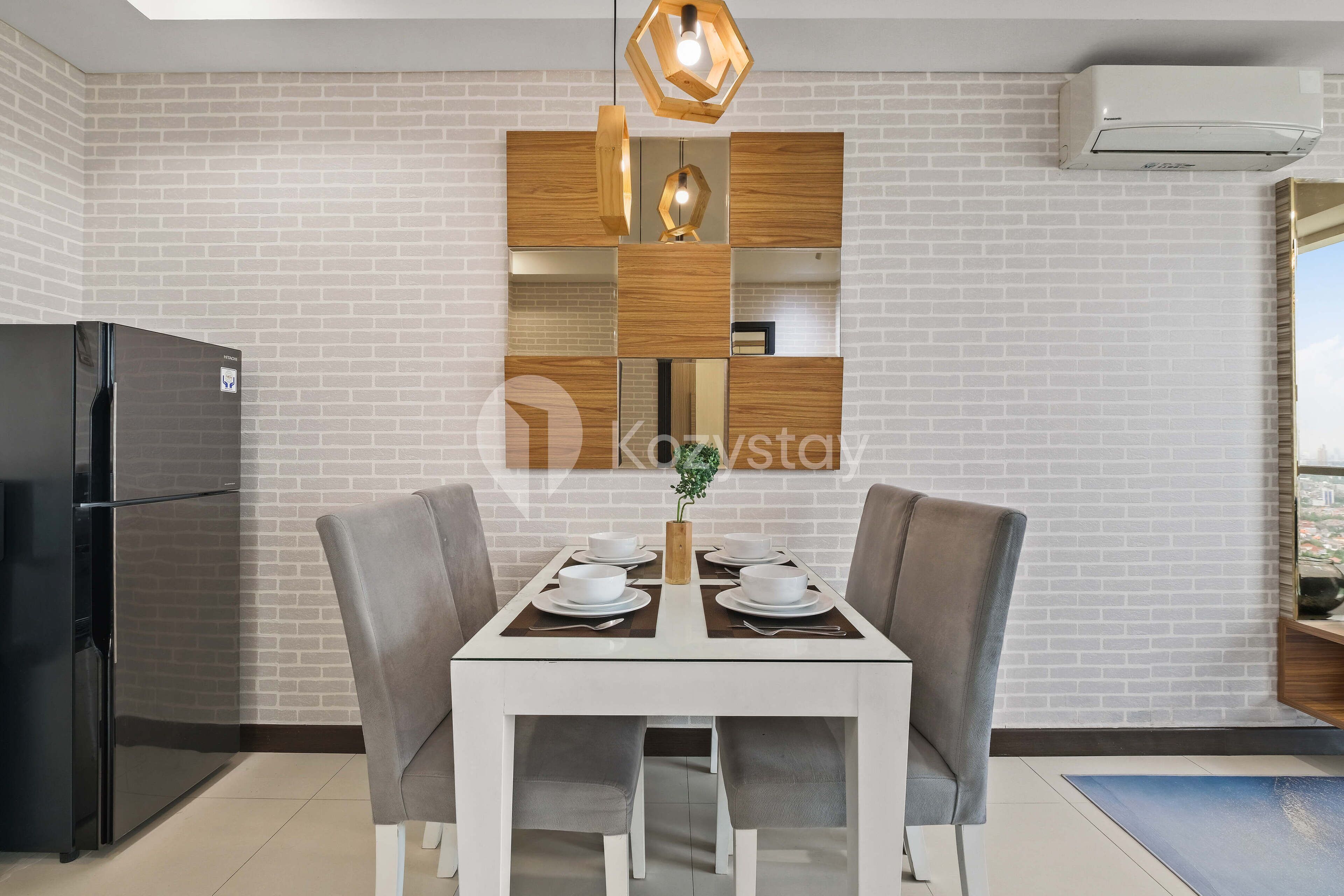 Una cocina moderna con pared de ladrillo blanco, un refrigerador negro, una mesa de comedor blanca con cuatro sillas y una estantería de madera sobre la mesa.