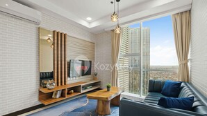Una sala de estar moderna con un televisor grande, estanterías de madera, una mesa de centro y un sofá con cojines azules.