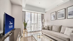 A modern hotel room with a flat-screen TV, a sofa, a glass coffee table, and framed artwork on the wall.