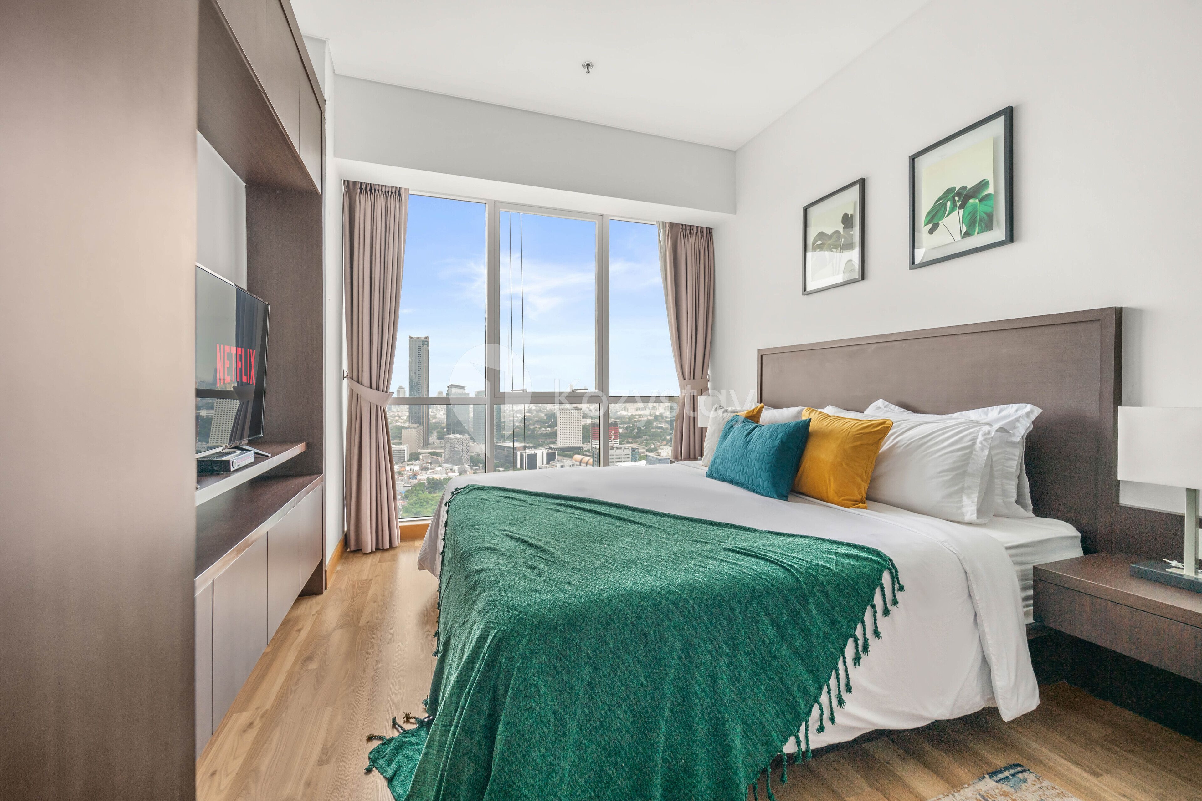 A modern hotel room with a large bed, a TV, a desk, and a view of the city.