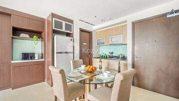 A modern kitchen with a microwave, refrigerator, and wooden cabinets. There is a dining area with a glass table and beige chairs.