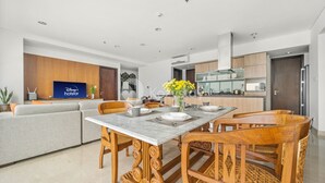 A modern living room with a grey sofa, a dining table with chairs, and a TV displaying 'Disney+ holostar'. - BUNGALOW by Kozystay (Jakarta)