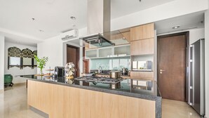 A modern kitchen with a central island, stainless steel appliances, wooden cabinets, and a green plant. - BUNGALOW by Kozystay (Jakarta)