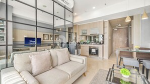 A modern living room with a sofa, a glass coffee table with a plant, and a kitchen area with a dining table and chairs. - QUARTER by Kozystay (Jakarta)