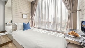 A modern hotel room with a bed, a laptop, and a croissant on the bedside table. - QUARTER by Kozystay (Jakarta)