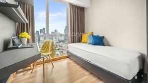A modern bedroom with a city view, a bed, a desk with a laptop, and a chair. - LONDON by Kozystay (Jakarta)