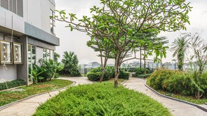 Un espace extérieur aménagé avec des arbres, des arbustes et un chemin menant à un bâtiment équipé de climatiseurs.