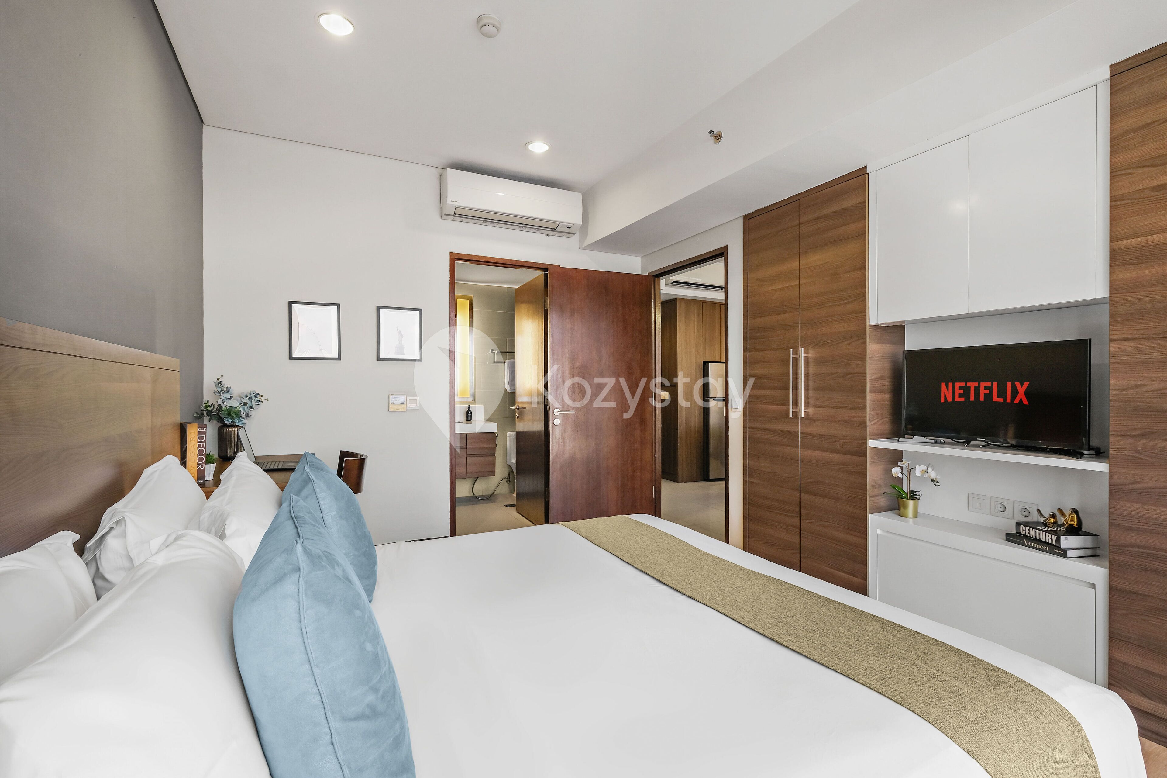 Quarto de hotel moderno com cama bem arrumada, televisão exibindo 'NETFLIX' e guarda-roupa de madeira.