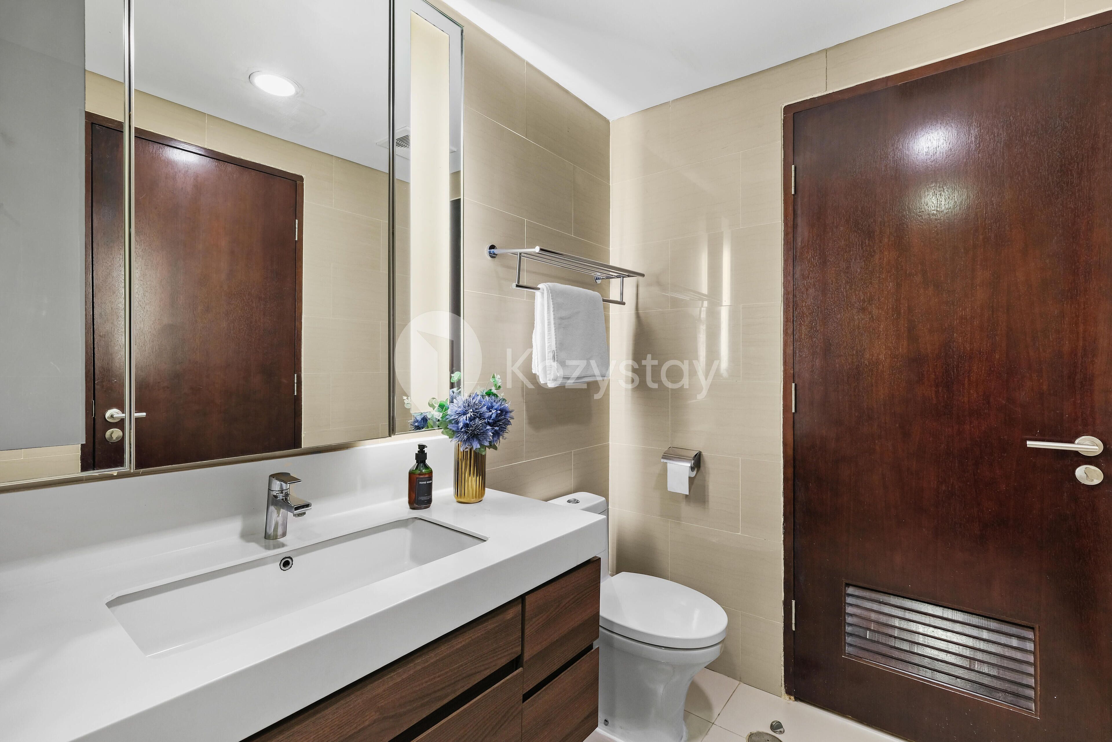 A modern bathroom with a large mirror, a white sink, a toilet, and a wooden door.