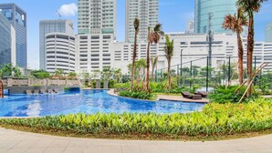 A swimming pool surrounded by greenery and palm trees, with modern buildings in the background. - MAPLE by Kozystay (Jakarta)