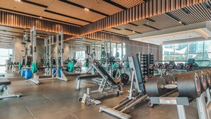 A modern gym with various exercise equipment, large windows, and a wooden ceiling. - CEDAR by Kozystay (Jakarta)