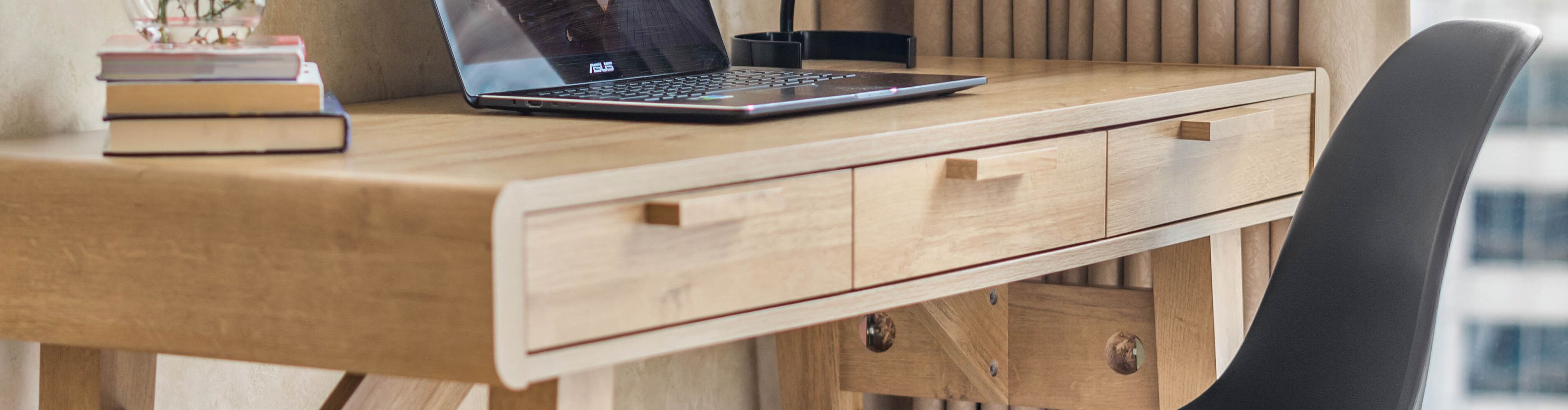 Ein Holztisch mit einem Laptop, Büchern und einem schwarzen Stuhl.