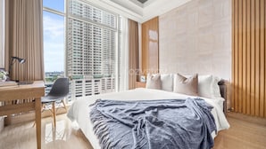 A modern hotel room with a large bed, a desk, and a chair. There is a view of tall buildings outside the window. - CEDAR by Kozystay (Jakarta)