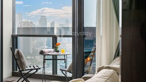 Un balcon avec vue sur la ville, une petite table avec un journal, une chaise et une plante en pot.