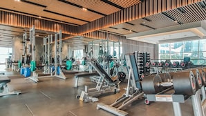 A modern gym with various exercise equipment, large windows, and a wooden ceiling. - HAVEN by Kozystay (Jakarta)