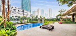 A swimming pool with lounge chairs, surrounded by greenery and modern buildings in the background.