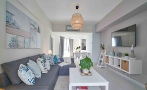 A modern living room with a grey sofa, white coffee table, and a large TV on the wall.