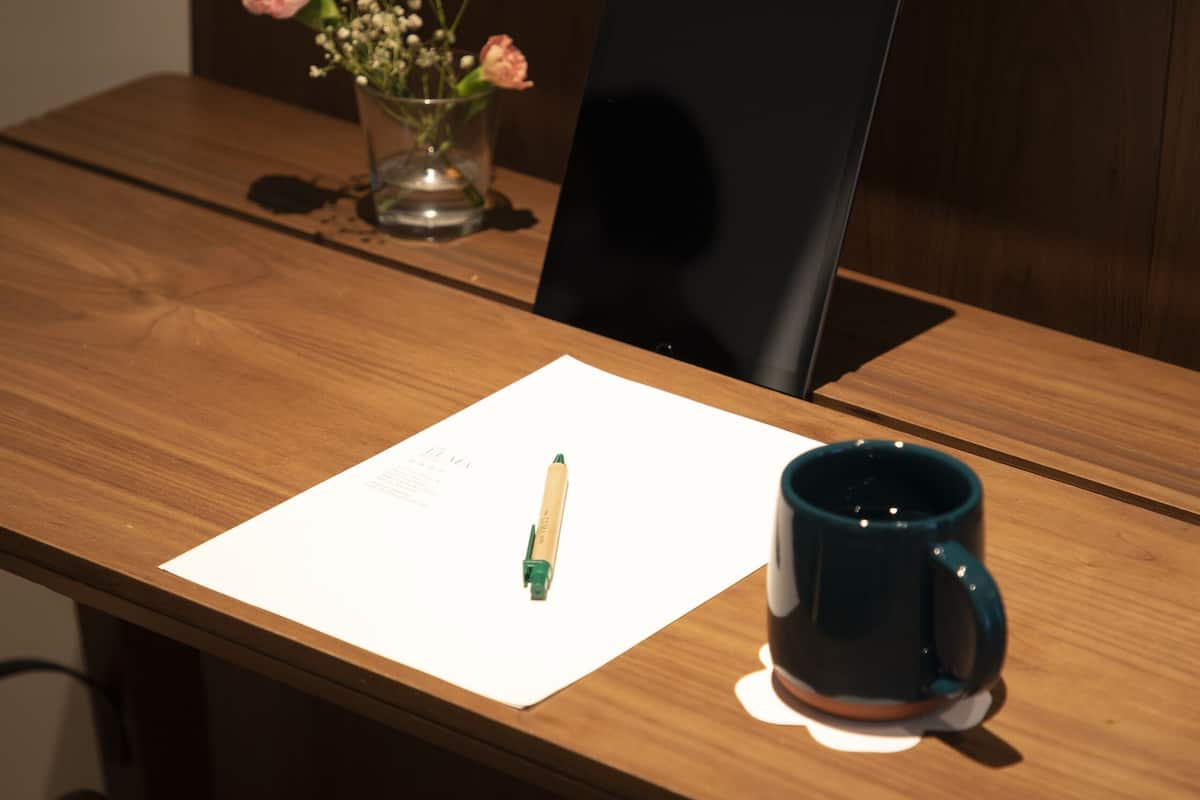 A wooden table with a laptop, a vase with flowers, a mug, and a piece of paper with a pen.