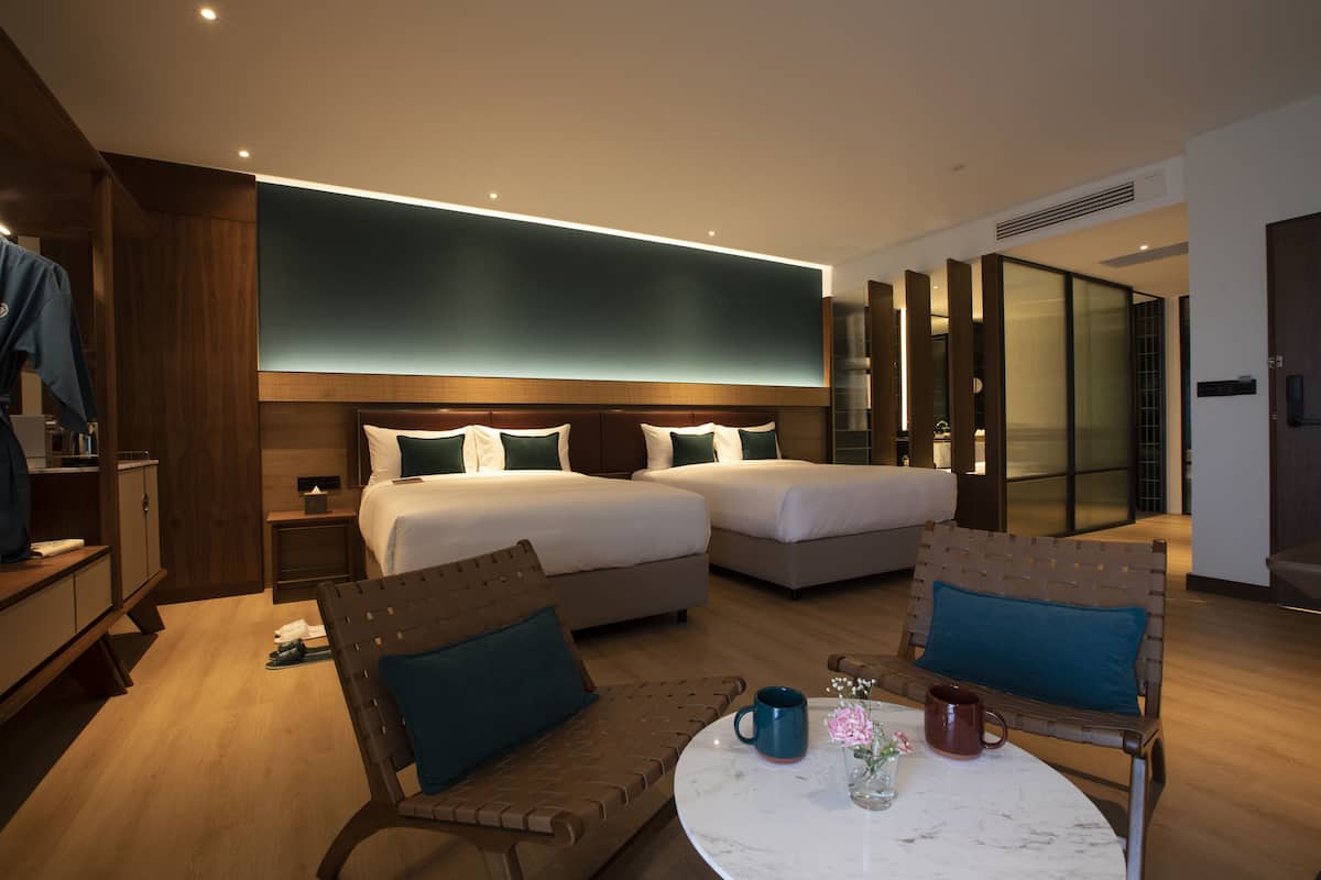 A modern hotel room with two beds, a round table with a vase of flowers, and a seating area with a chair and a table.