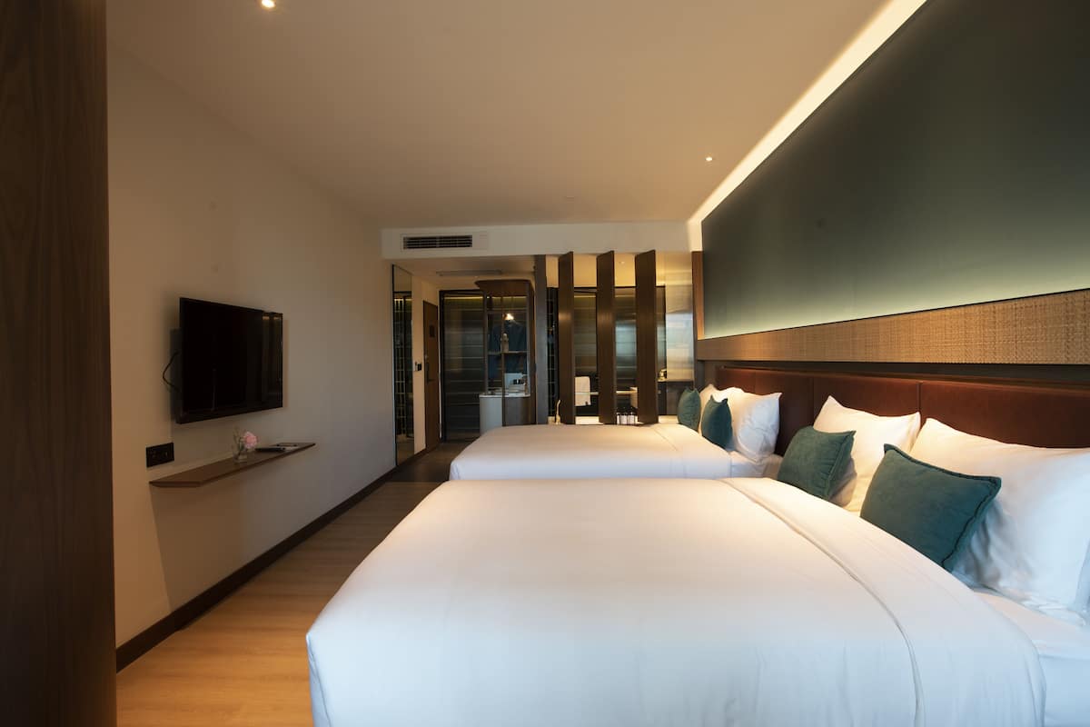 A hotel room with two beds, a flat-screen TV mounted on the wall, and a wooden floor.