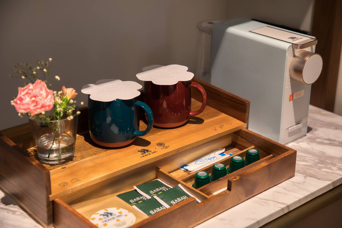A wooden tray with two mugs, a vase with flowers, and a drawer with sachets on a marble countertop.