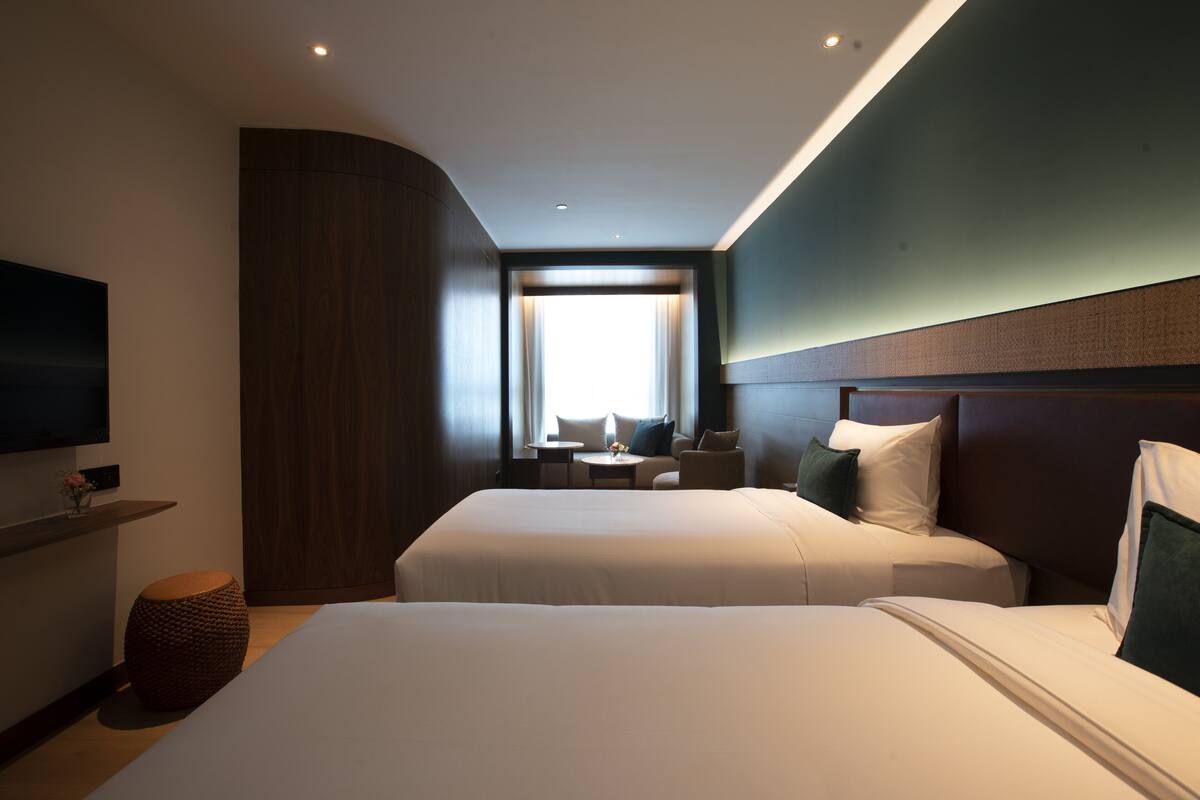 A hotel room with two beds, a TV, a small table, and a window with curtains.