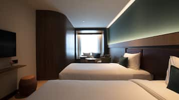 A hotel room with two beds, a TV, a small table, and a window with curtains.