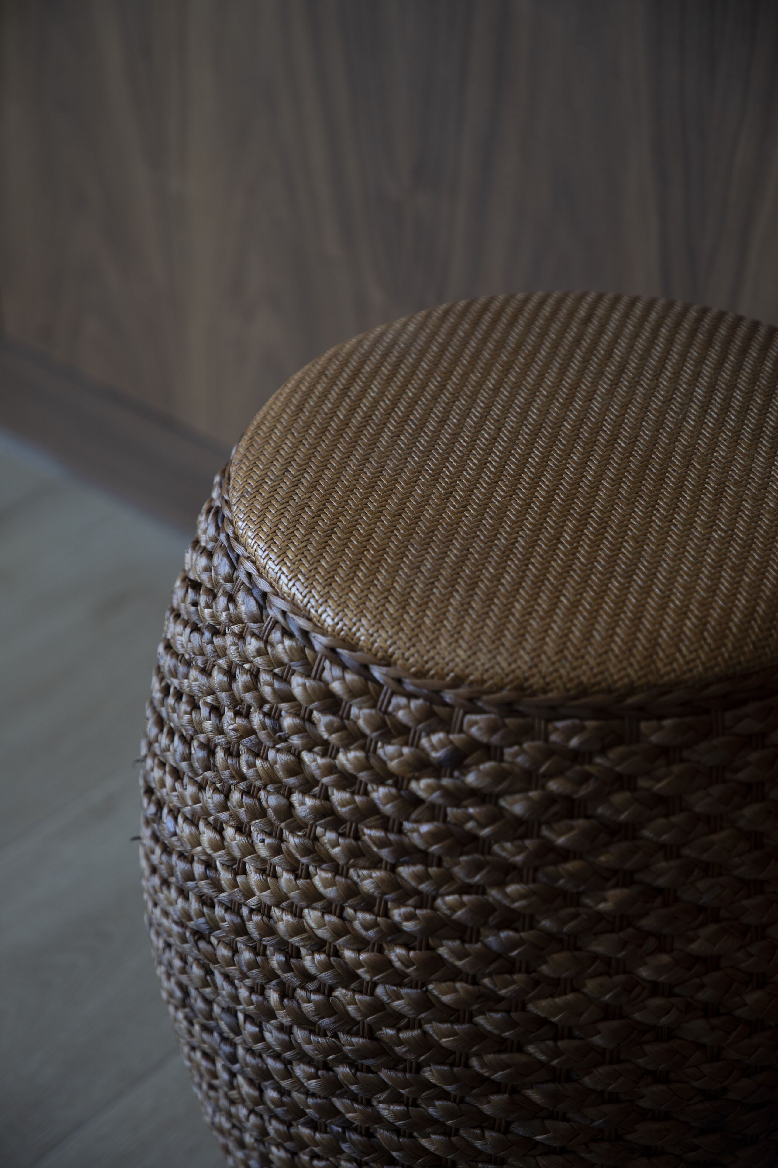 A woven wicker ottoman with a cylindrical shape and a textured surface.