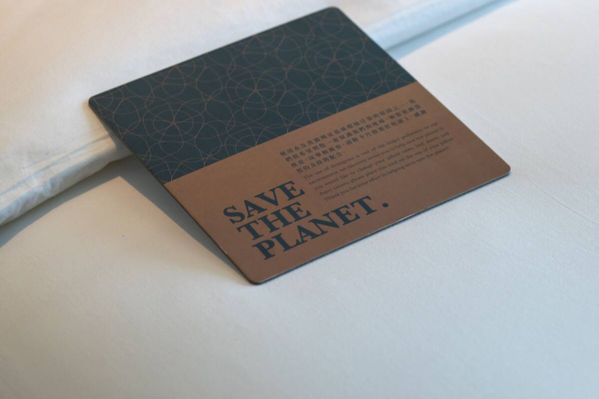 A neatly made bed with a pillow and a card on it that reads "SAVE THE PLANET."