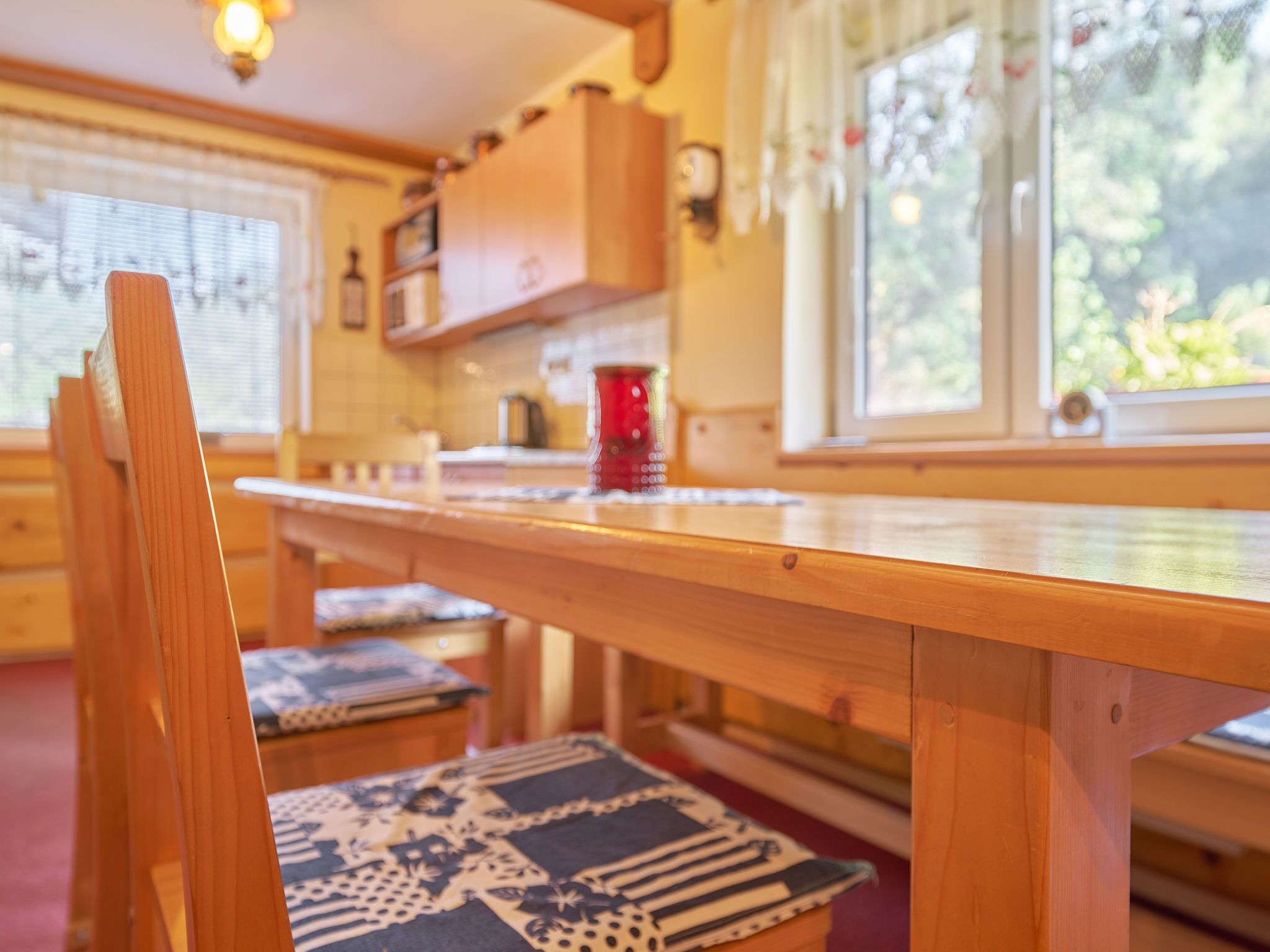 A wooden dining table with chairs, a red cup, and a window with a view of greenery.
