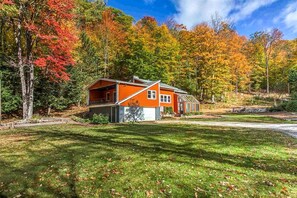 Une maison à deux étages avec un garage, entourée d’une pelouse bien entretenue et d’arbres aux couleurs automnales.