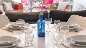 Una mesa de comedor dispuesta con platos, vasos y cubiertos, con un jarrón azul en el centro que contiene flores secas.