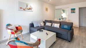 Una sala moderna con un sofá seccional gris, una mesa de centro blanca y un sillón colorido.