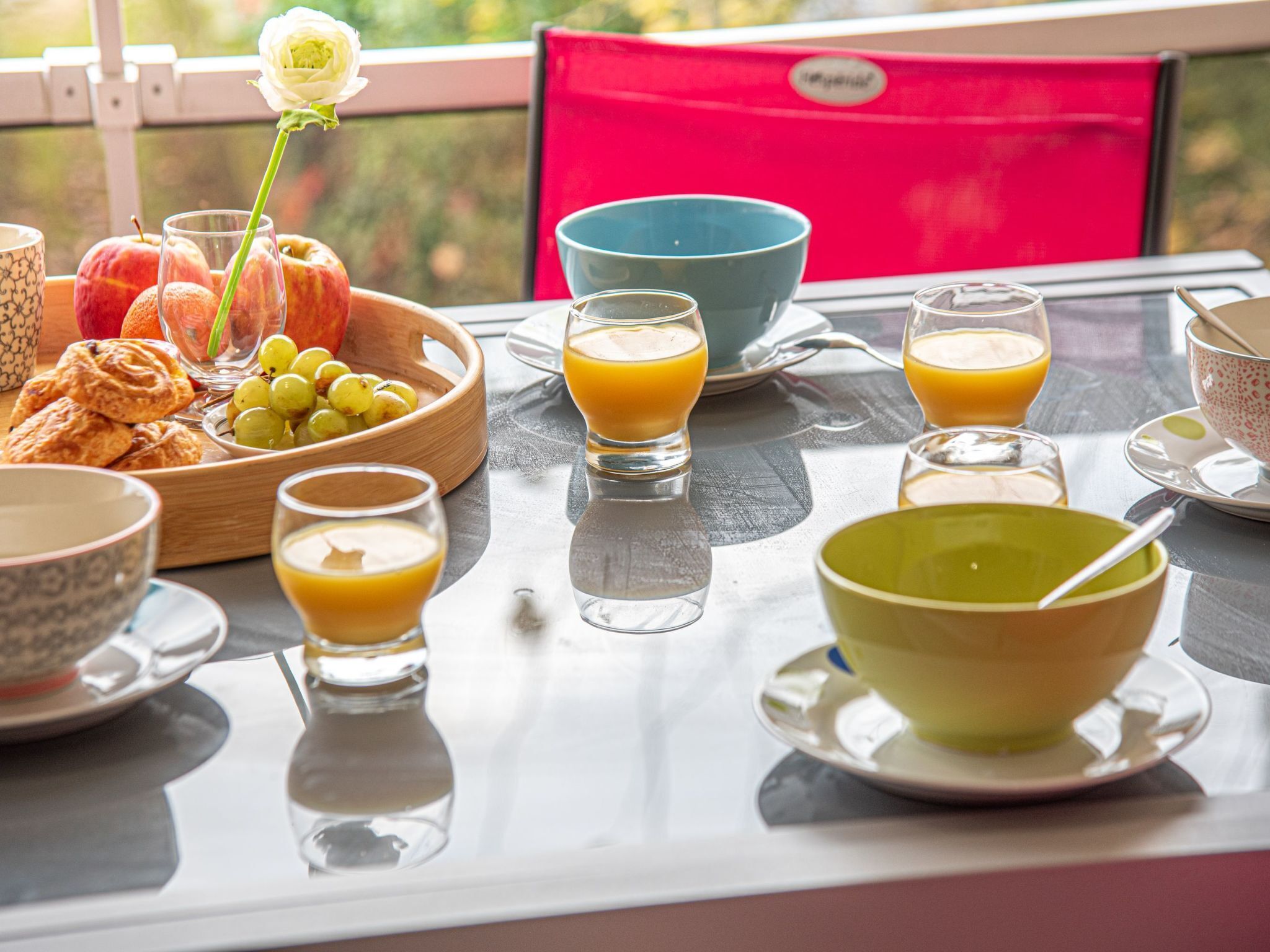 A breakfast table with a variety of fruits, pastries, and beverages, including a bowl of grapes, a plate of croissants, and glasses of orange juice.
