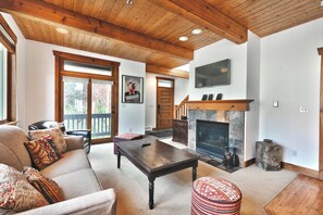 Un salon spacieux doté d’une cheminée, d’un plafond en bois et d’une grande fenêtre.